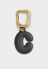 Charm Untags per iPhone a forma di lettera C, effetto pelle in colore nero, con moschettone per attaccare l’accessorio alla cover