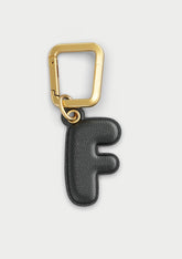 Charm Untags per iPhone a forma di lettera F, effetto pelle in colore nero, con moschettone per attaccare l’accessorio alla cover