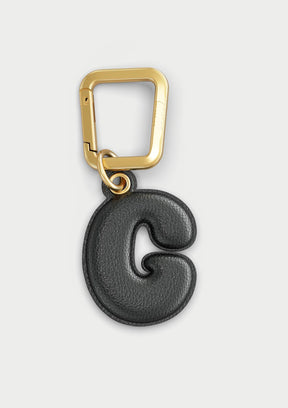 Charm Untags per iPhone a forma di lettera G, effetto pelle in colore nero, con moschettone per attaccare l’accessorio alla cover