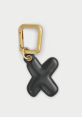 Charm Untags per iPhone a forma di lettera X, effetto pelle in colore nero, con moschettone per attaccare l’accessorio alla cover